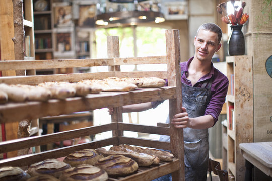 Portrait Of Young Male Baker With Shelves Of Fresh Bread