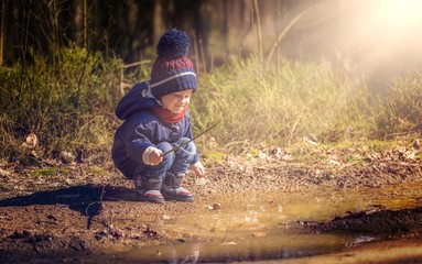 Little boy playing in puddle in spring forest.