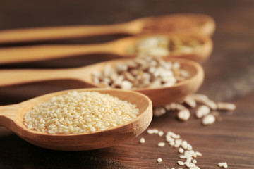 Sesame, flax, pumpkin and sunflower seeds in wooden spoons on table, closeup
