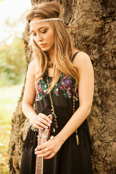 Hippy woman with guitar looking sad standing by tree