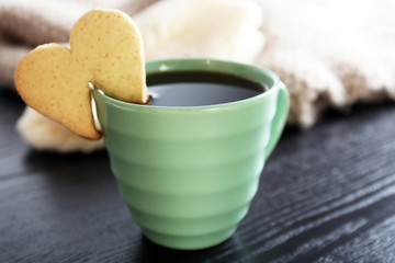 Heart shape cookie on cup of coffee on wooden table closeup