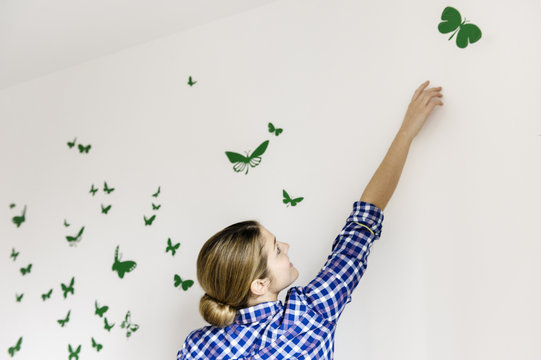 Young woman decorating wall with green butterflies