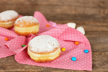 Delicious sugary donuts with pink napkin on wooden background