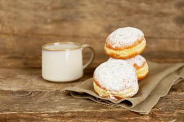 Delicious sugary donuts with cup of coffee on wooden background