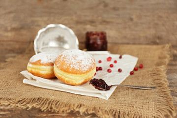 Delicious donuts with jam on parchment and sackcloth on wooden background