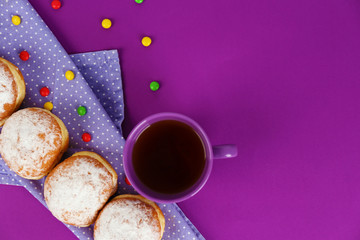 Delicious donuts with powdered sugar and cup of tea on purple surface, top view