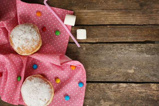 Delicious sugary donuts with pink napkin on wooden table, top view