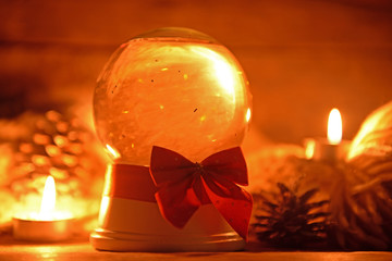 Christmas snow globe with ribbon bow in candlelight on wooden table closeup