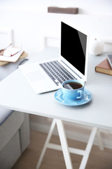 Modern interior. Comfortable workplace. Table with laptop and cup of coffee on it, close up