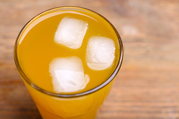 Glass of orange juice with ice block on wooden background, close up