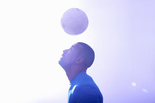 Studio shot of young male soccer player keeping ball mid air with header