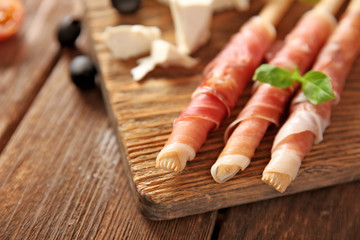 Bread sticks grissini with prosciutto ham on a  wooden board, close up