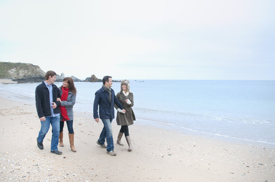 Two adult couples walking on beach, Thurlestone, Devon, UK