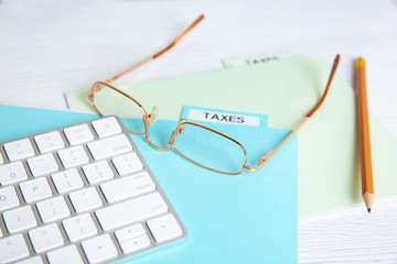 Folder with tax documents, glasses, pencil and keyboard on white wooden table