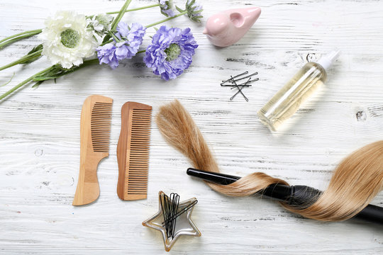 Strand of hair with flowers, barber equipment and tools on light wooden background