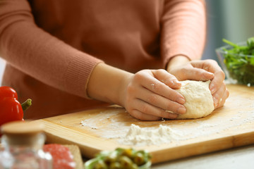 Woman making a pizza dough on a wooden board, close up