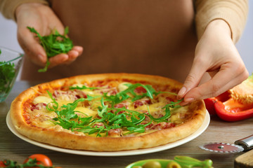Woman decorating fresh baked pizza with arugula, close up