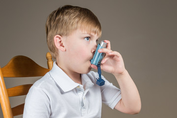Young boy with asthma using a blue inhaler