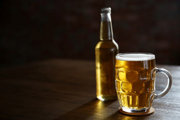 Glass mug of light beer with bottle on wooden table