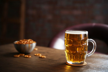Glass mug of light beer with snacks on wooden table