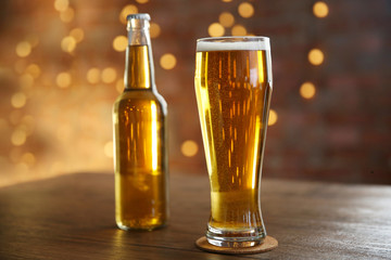 Glass of light beer with bottle on wooden table over glitter background