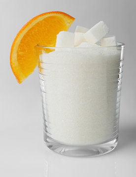Old fashioned glass with lump, granulated sugar and slice of orange on grey background