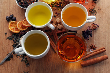 Cups with different kinds of tea and ingredients on table