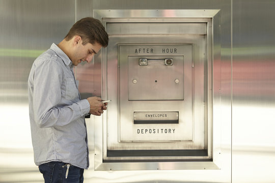 Mid adult man banking on cellphone next to bank deposit box