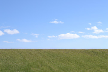 Grass and the sky. Background. 
The slope of the dam, covered with spring grass. Blue sky with clouds.