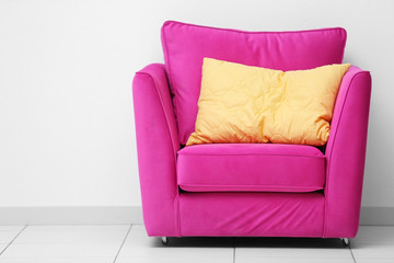 Pink armchair with yellow pillow on white wall background