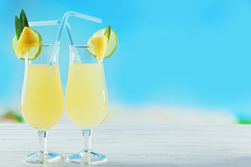 Glasses of fresh pineapple cocktail on blue background