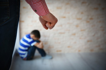 Father fist as punishment and little boy sitting on floor indoors