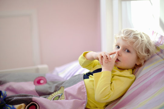 Male toddler lying in bed making secret hand gesture sign