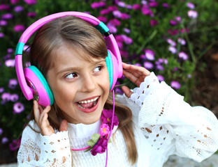  Happy smiling girl with long blond hair, lace clothes listening to music on headphones on a purple blossom flowers background