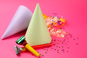Two dotted Birthday hats with serpentine streamer and noise makers on pink background