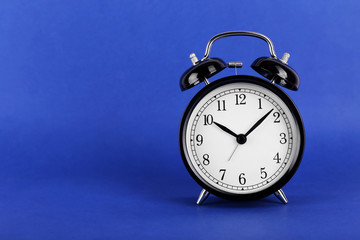 Black retro alarm clock on blue background