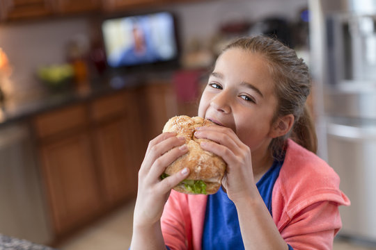 Girl in kitchen biting sandwich