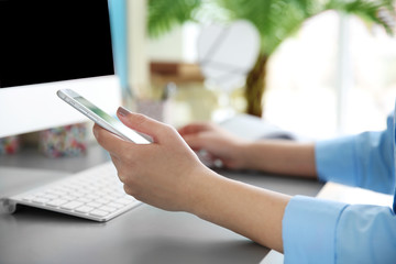 Woman working with smartphone and computer indoors