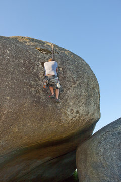 Young man climbing with ropes on boulder