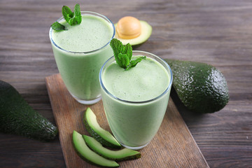 Avocado smoothie with green leaves on wooden background