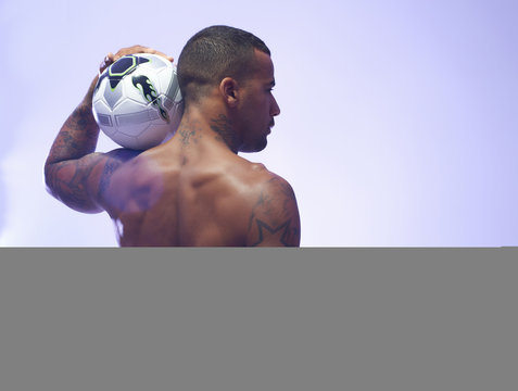 Studio shot of young male soccer player holding up ball on shoulder