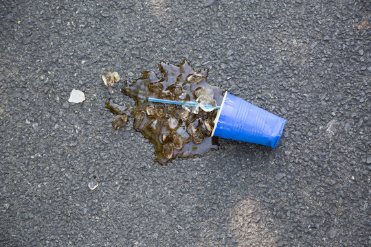 Spilled soft drink with plastic cup and ice cubes on tarmac