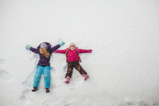 Two sisters playing, making snow angels in snow