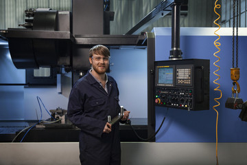 Apprentice holding a u-bolt strap in front of CNC machine