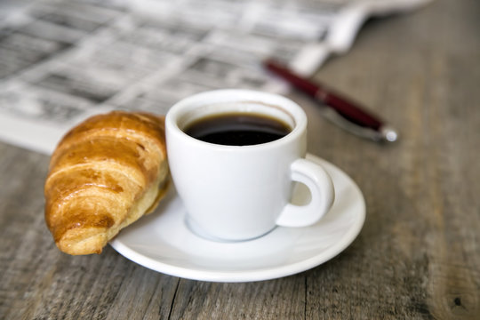Coffee with croissant and newspaper with pen