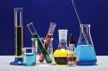 Chemical lab glassware: graduated cylinder, small beaker, beaker with two test tubes, flat-bottom flask, dropper bottle, Erlenmeyer flask with stirring rod
