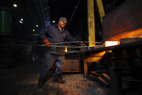 Forge worker removes red hot steel billet from furnace for forging into crank shaft