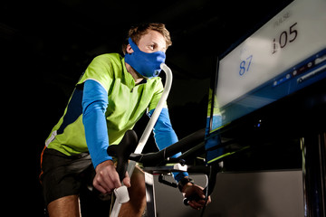 Young man in face mask on gym exercise cycle in altitude centre