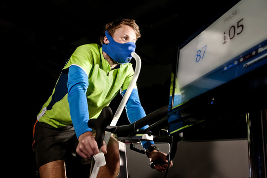 Young man in face mask on gym exercise cycle in altitude centre