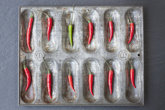 Large group of red chillies and one green chilli ordered in baking tin